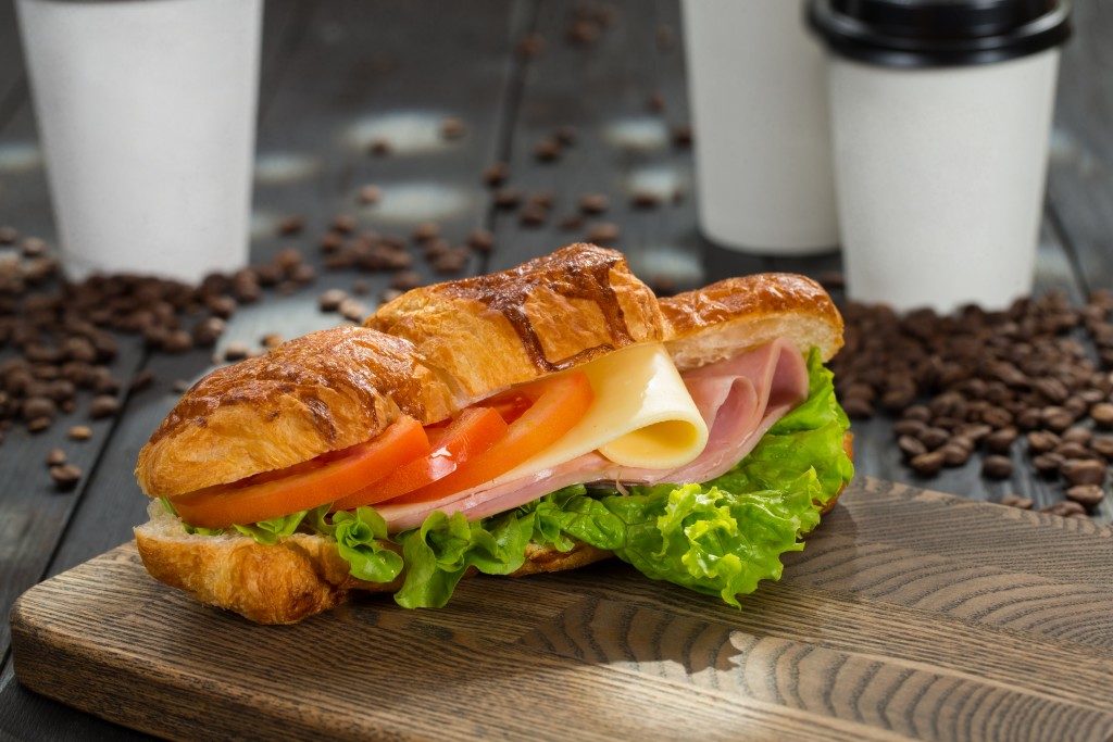 Croissant sandwich with ham, cheese and tomatoes on wooden cutting board