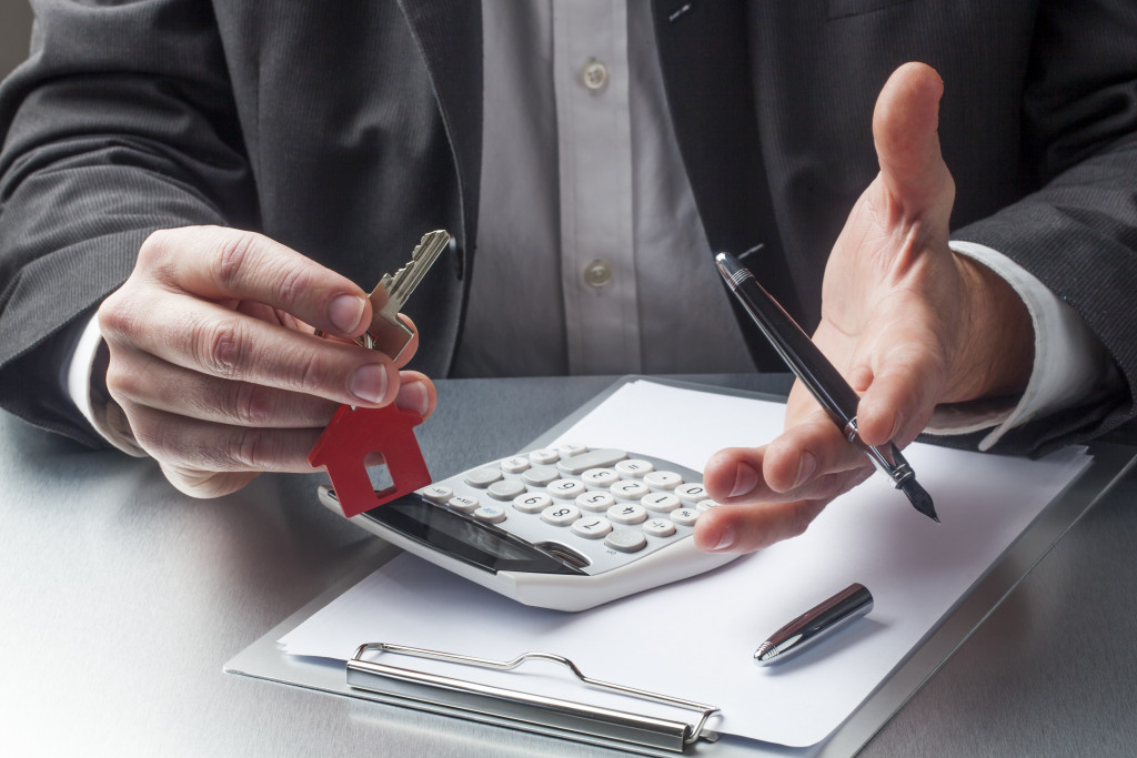 businessman holding house key and pen with calculator and document on a clipboard on the table