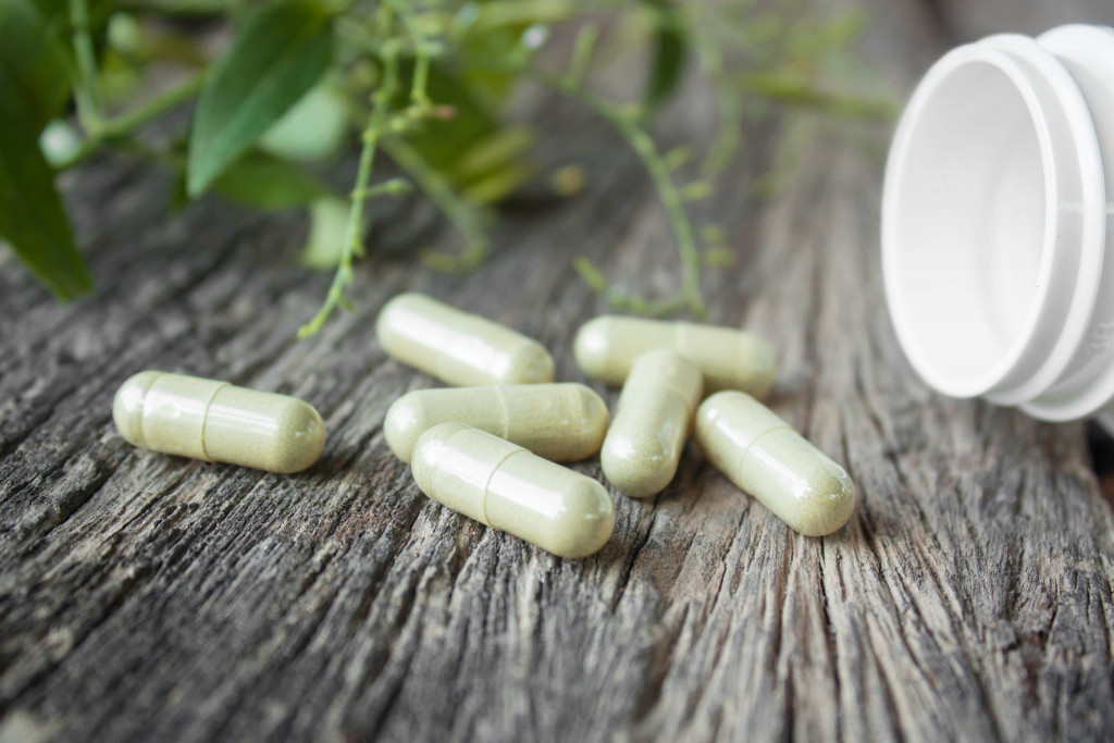 green capsules with the bottle and herbal leaf beside it